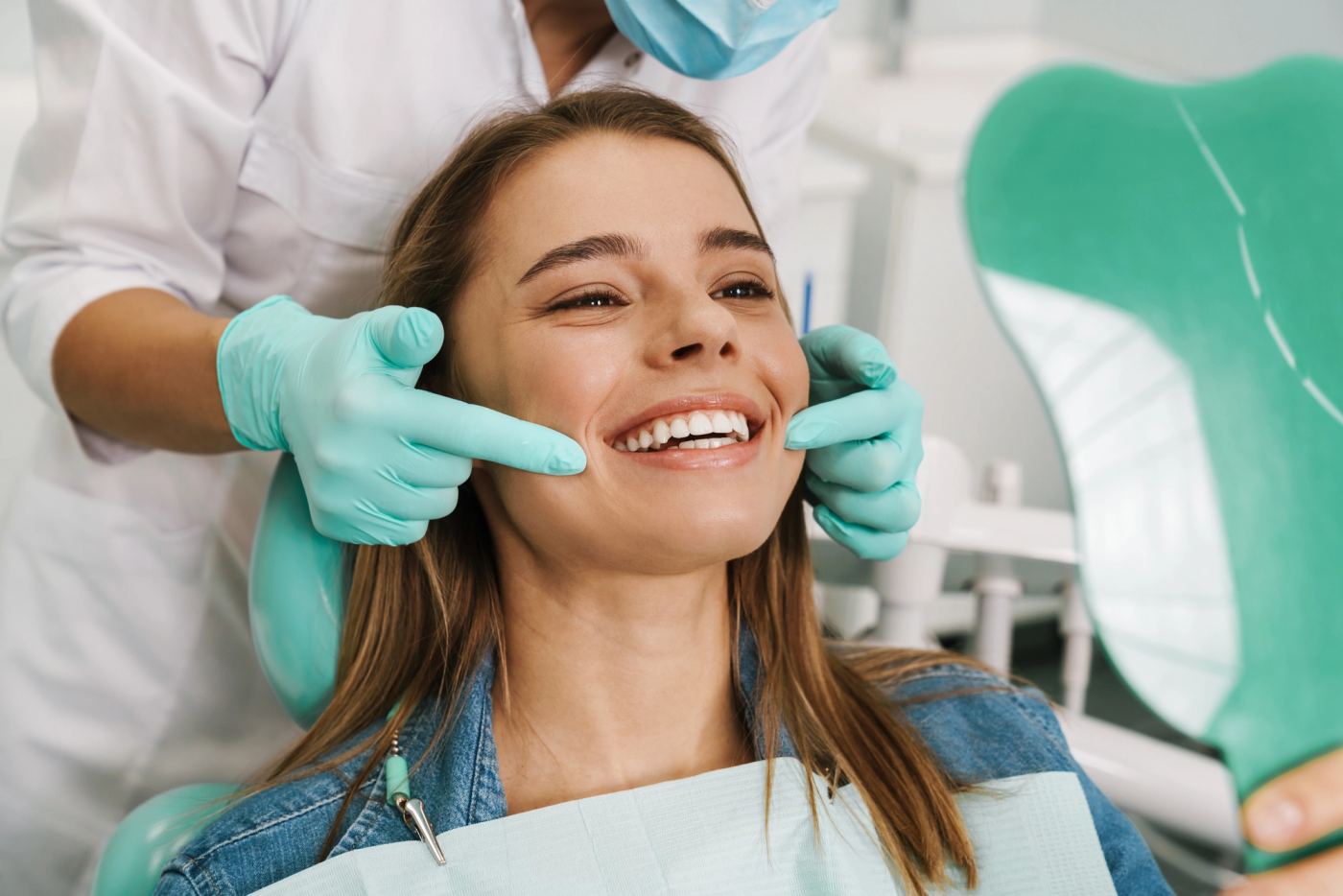 Smiling woman in a dental chair looking at her bright teeth in a mirror, assisted by a dentist.