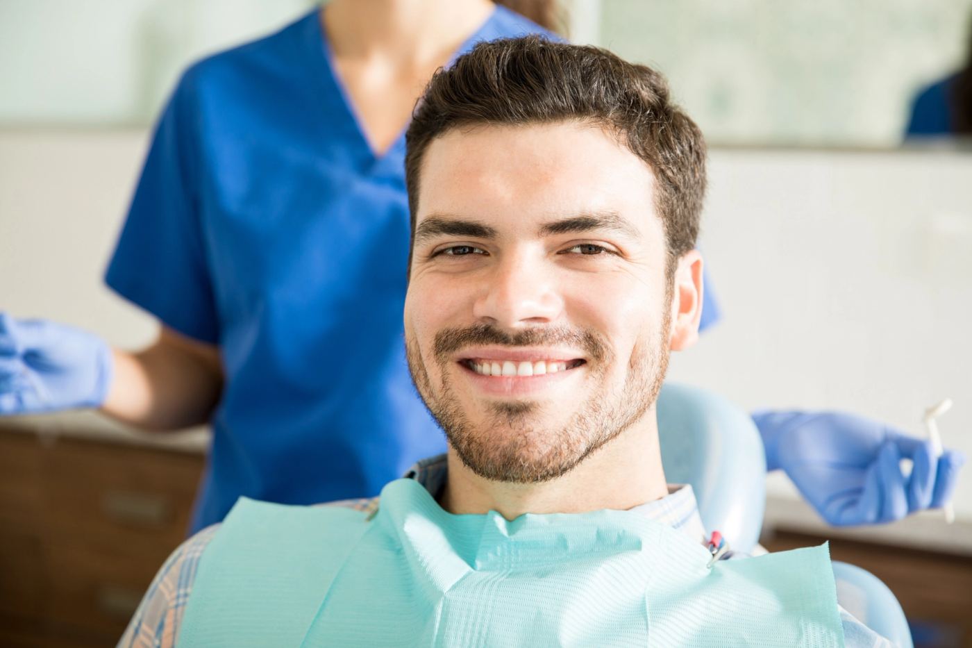 A man with a dental bib smiles in a dentist's chair.